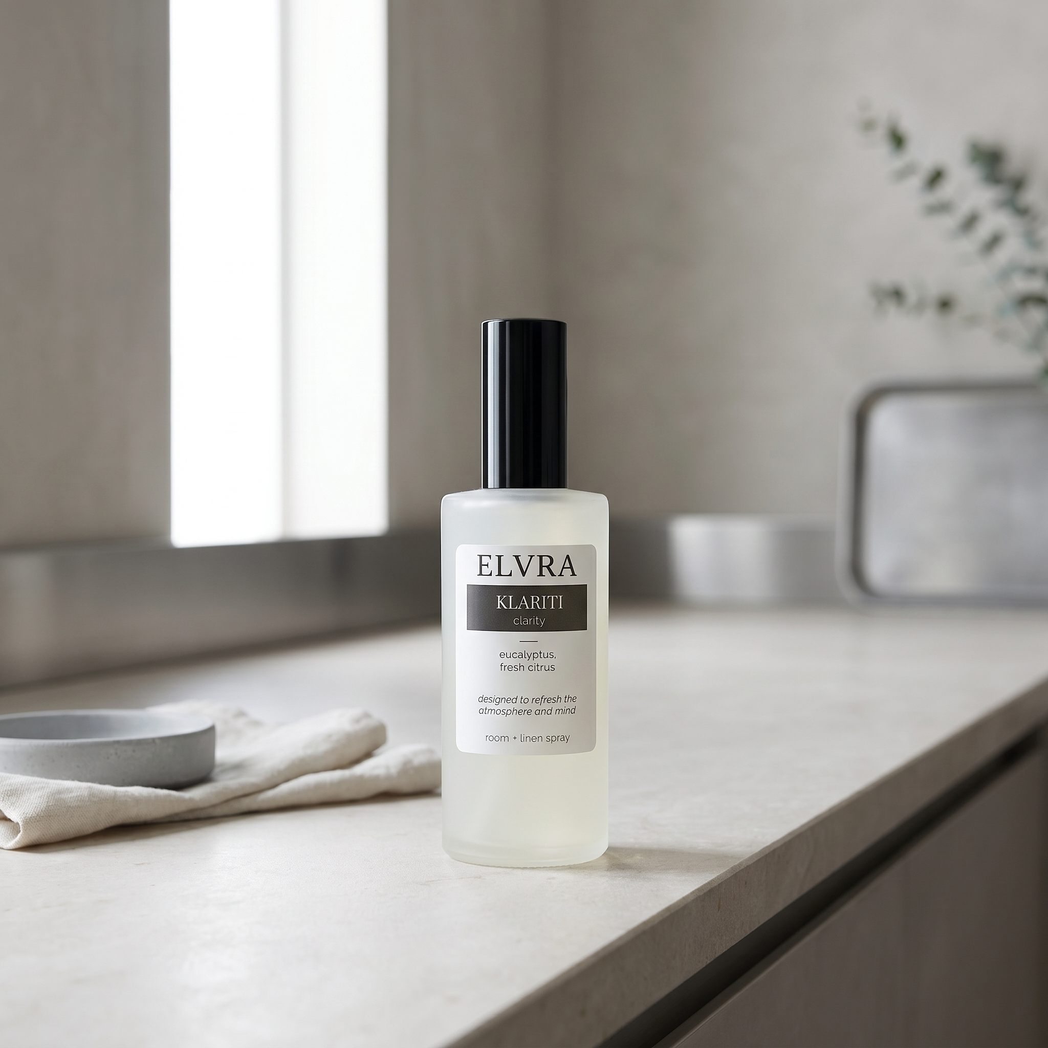 Frosted Elvra Klariti Atmosphere and linen mist bottle on pale stone in a serene, minimalist daylight interior.