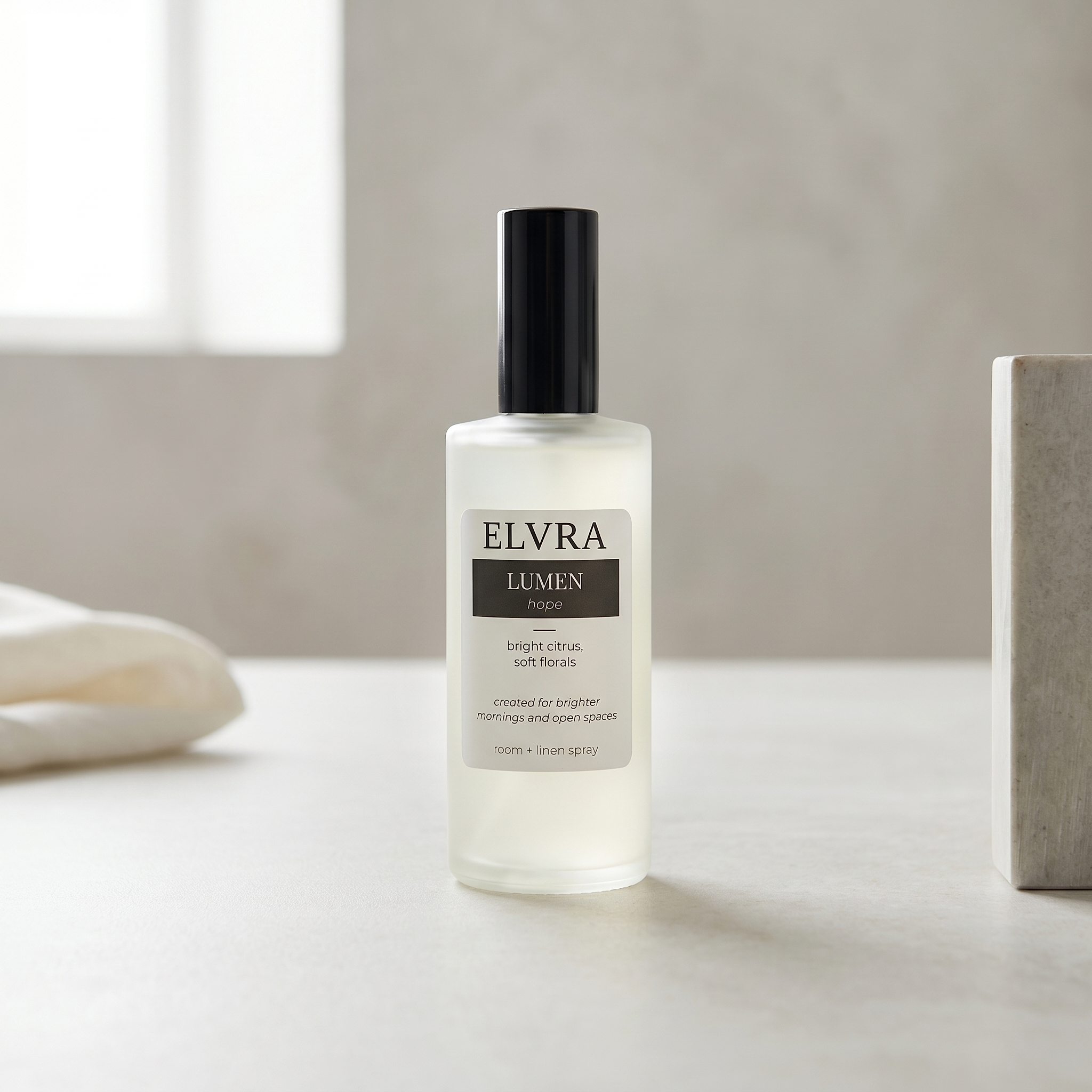 Centered Elvra Lumen room and linen mist bottle on matte stone with soft white studio light and faint linen and plaster accents.