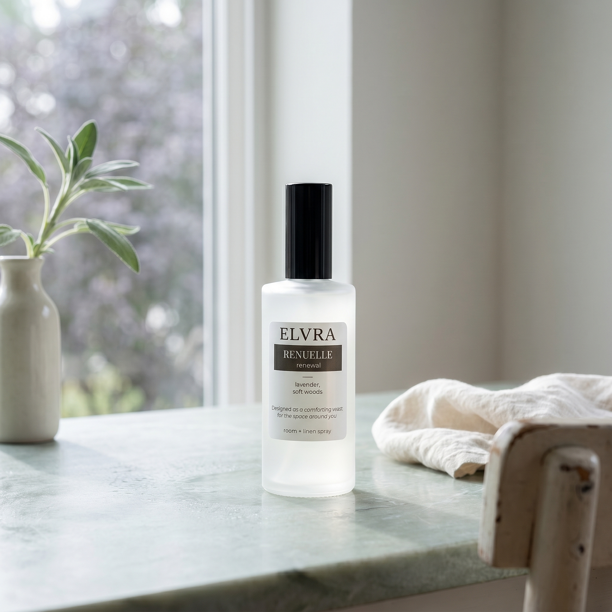 Frosted Elvra Renuelle atmosphere mist bottle on pale stone beside linen and sage in soft post-rain daylight.