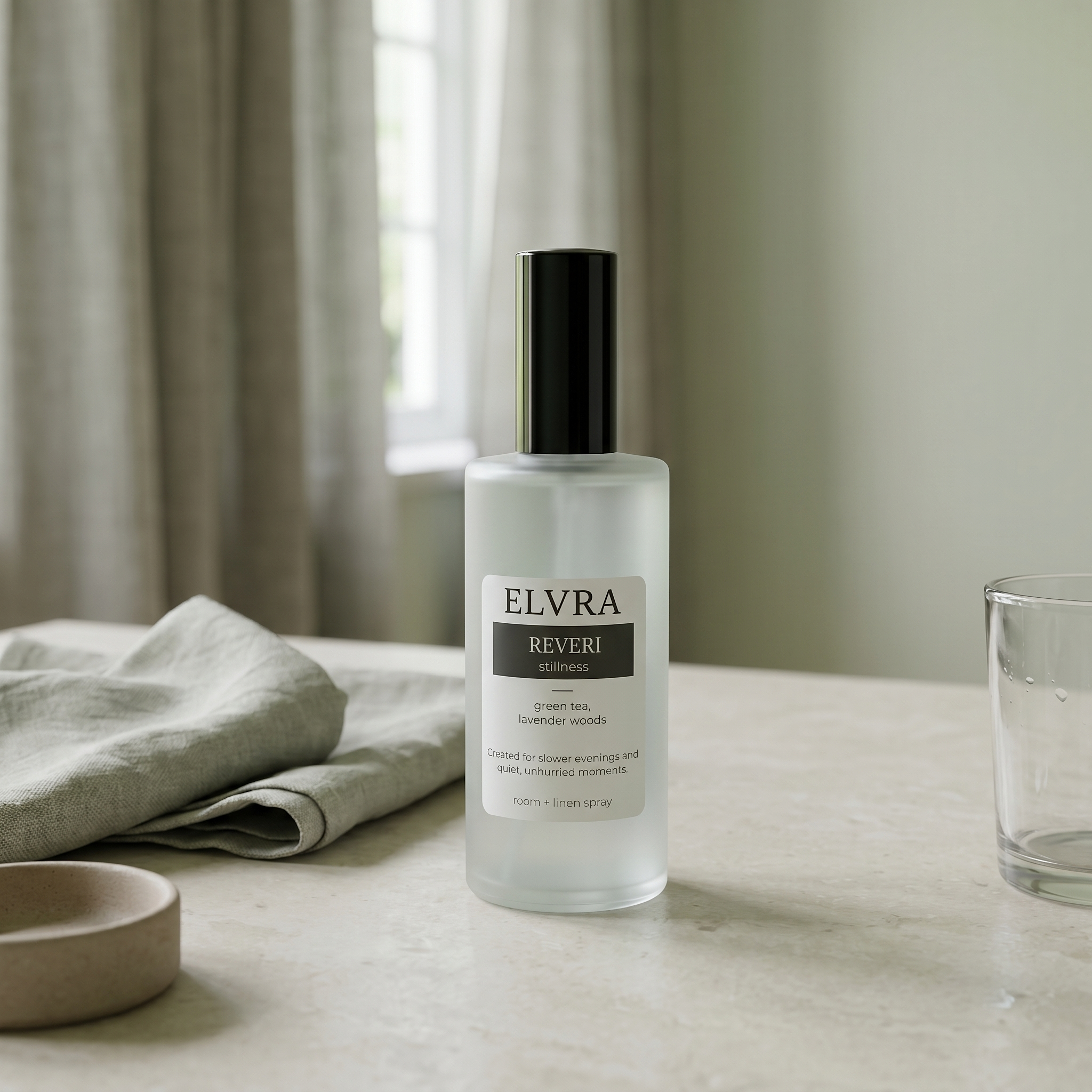 Frosted Elvra Reveri atmosphere mist for room and linen on pale stone with soft daylight, linen curtains, and muted green interior tones.