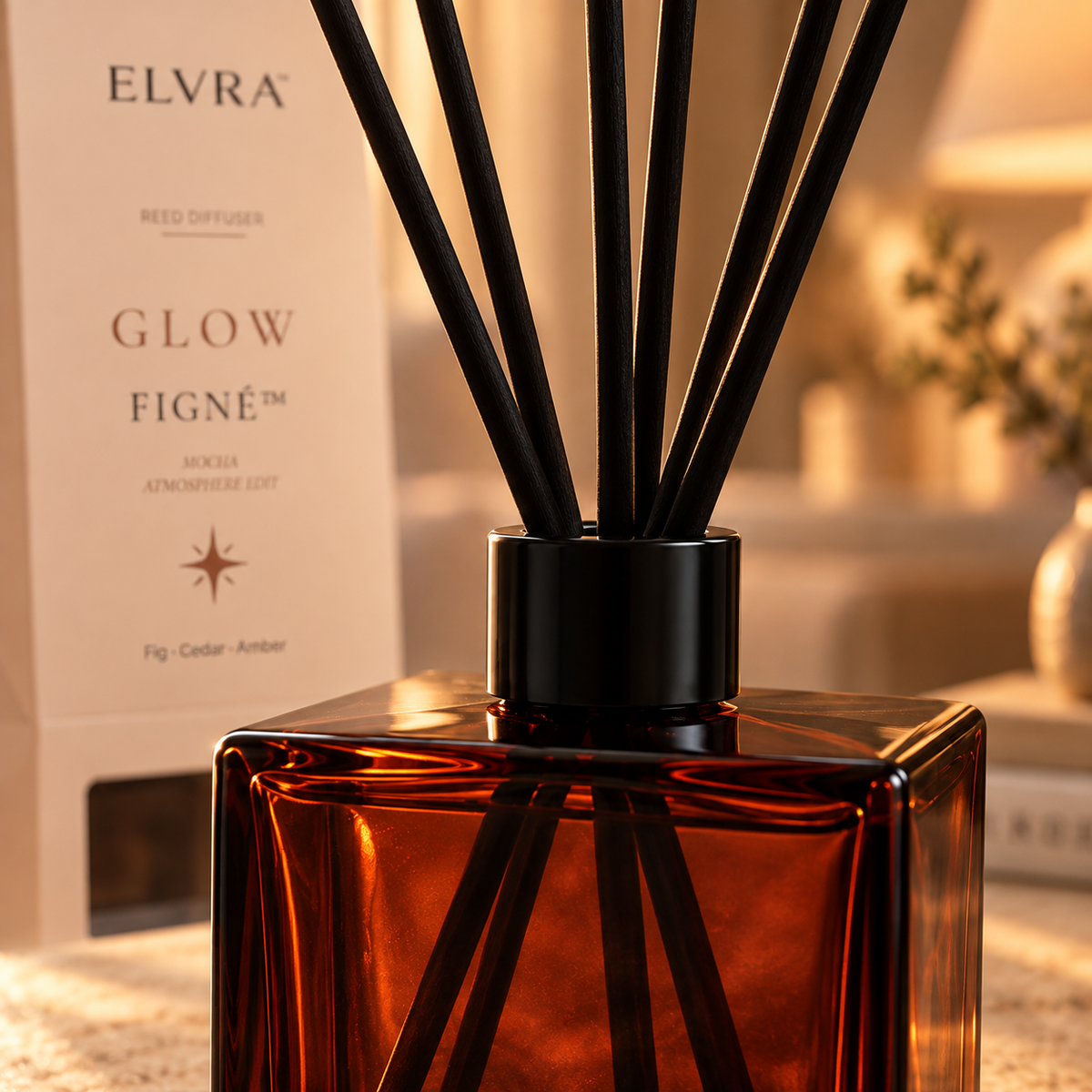 Close-up of the ELVRA Figné Glow reed diffuser showing the burgundy glass bottle, matte black collar, and black fiber reeds.