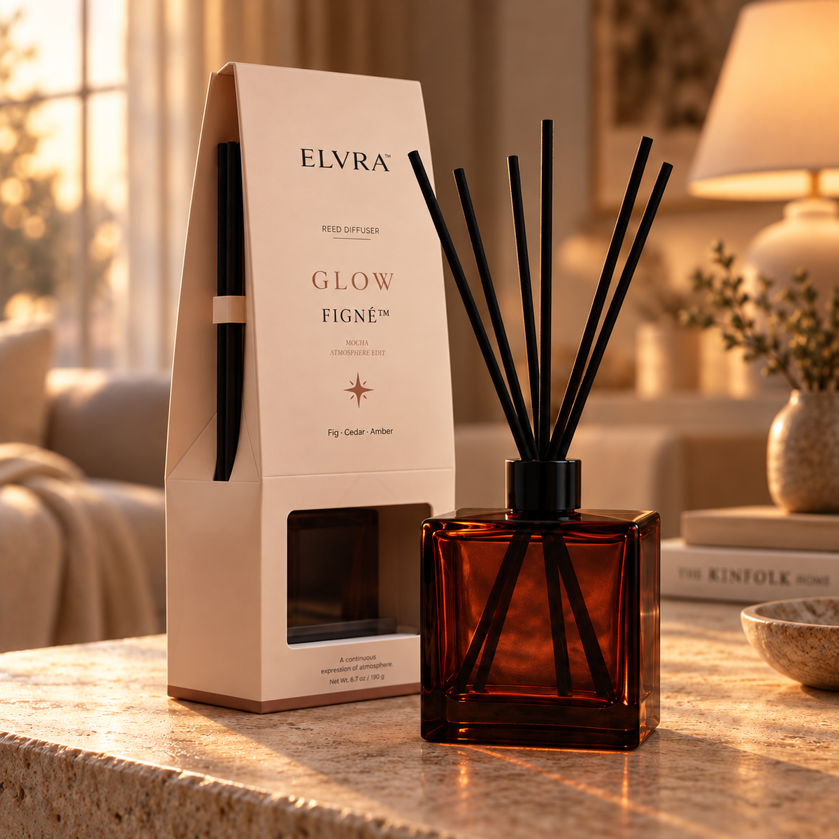 ELVRA Figné Glow reed diffuser in a burgundy glass bottle with black reeds and matching Mocha Atmosphere Edit packaging in warm golden light.