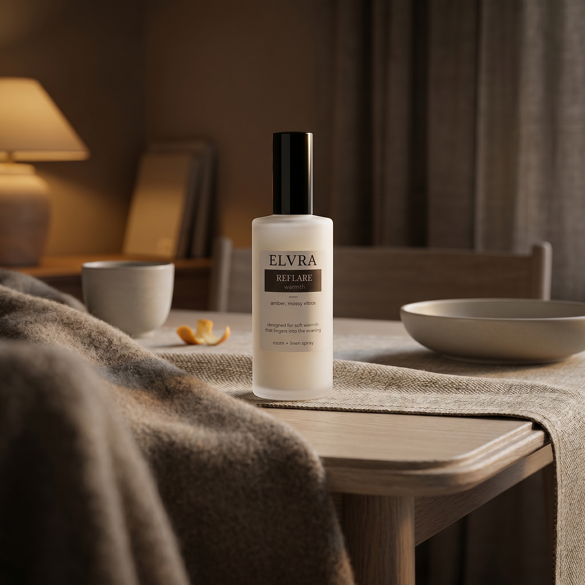Frosted Elvra Reflare Atmosphere & Linen Mist bottle with black cap on a linen-draped tabletop in soft amber evening light.