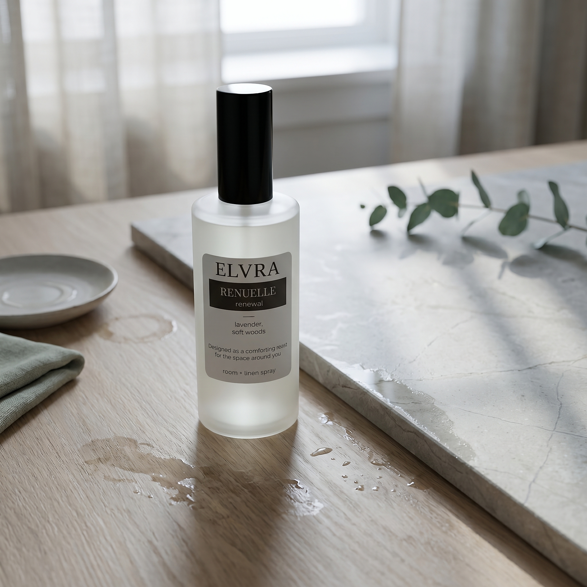 Elvra RENUELLE Atmosphere & Linen Mist on pale wood and stone with sage linen, eucalyptus, and soft after-rain daylight.