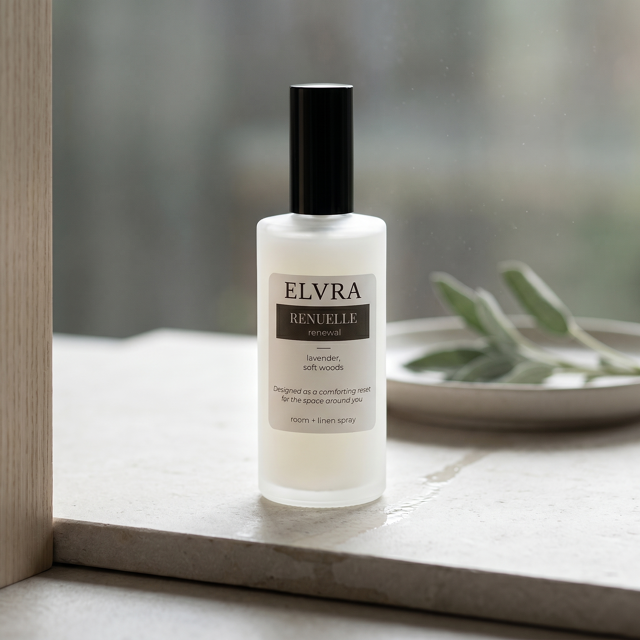 Frosted Elvra RENUELLE atmosphere mist bottle on damp limestone near a window with soft morning light and subtle sage accents.