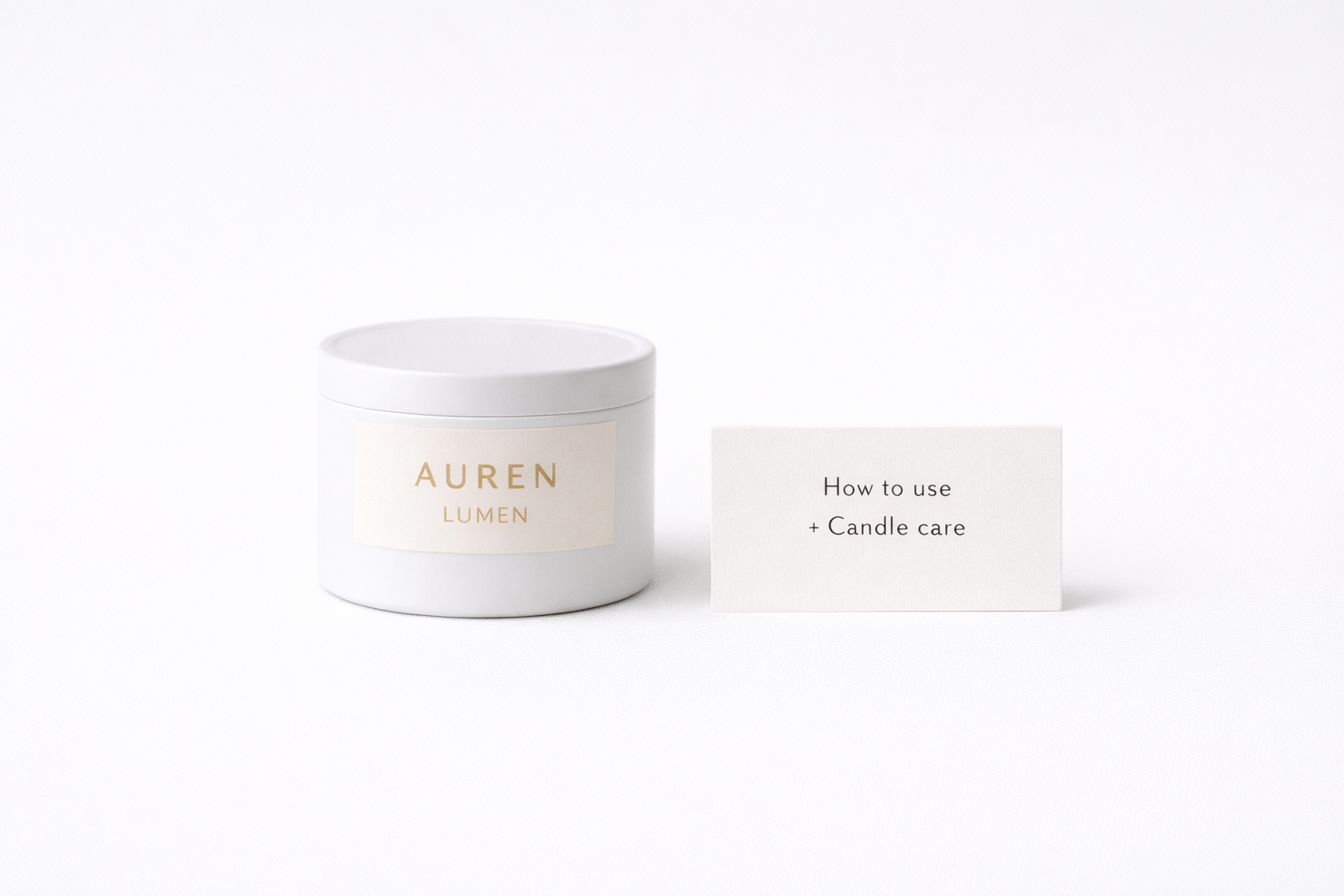 AUREN LUMEN discovery candle in a minimalist white travel tin, shown on a neutral surface beside a simple candle-care card